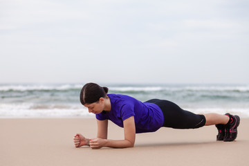 Fototapeta na wymiar Female athlete executing the plank exercise at the beach on an Autumn day.