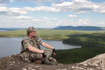 Man tourist on the top of the mountain sits cross-legged meditating resting, landscape Mountain lake sky background