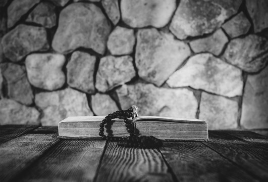 prayer beads with a cross on an open old book on old wooden table on a background of stone walls. selective focus, black & white photo. with space for your text