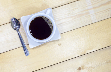 Top view of black coffee in a white ceramic coffee cup and stainless spoon on the wooden floor.