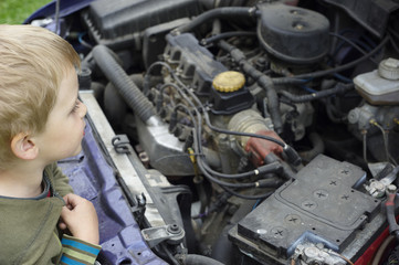 Little boy in front of open engine compartment doing some maintenance work at the car/ Little Mechanic