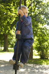 Little child blond boy climbing rope on the playground outdoors
