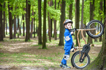 Naklejka premium Happy kid boy of 4 years having fun in autumn or summer forest with a bicycle