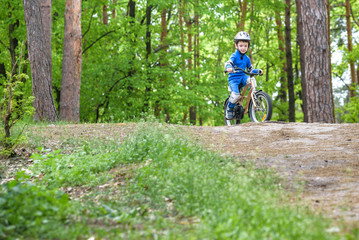 Naklejka premium Happy funny little kid boy in colorful raincoat riding his first bike on cold day in forest. Active leisure for children outdoors. carefree childhood concept