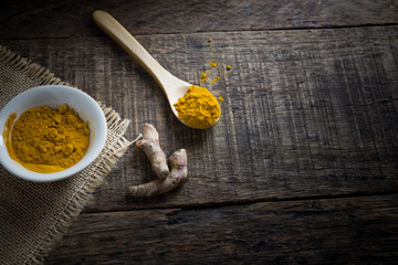turmeric powder in spoon and roots on wooden table