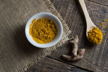 turmeric powder in spoon and roots on wooden table