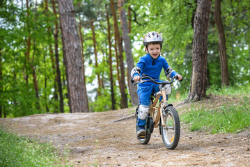 Fototapeta premium Happy funny little kid boy in colorful raincoat riding his first bike on cold day in forest. Active leisure for children outdoors. carefree childhood concept