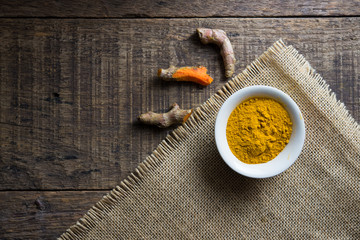 fresh turmeric roots and turmeric powder on wooden table