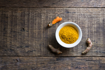 fresh turmeric roots and turmeric powder on wooden table