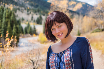 Portrait of young happy smiling woman by golden autumn river in Silverton, Colorado