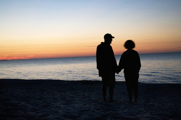 Couple holding hands at sunset on a beach.