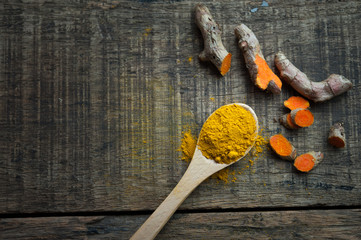 turmeric powder in spoon and roots on wooden table