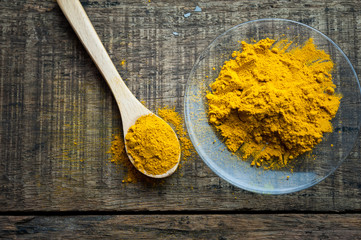 turmeric powder in spoon and roots on wooden table