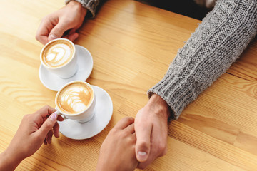 hands of the couple on a wooden table with coffee