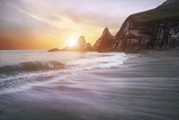 Stunning dramatic sunrise over beach with jagged rocks coastline
