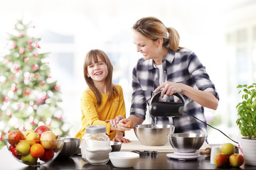 Mother and daughter at christmas.Portrait of cute daughter and her mom baking christmas cookies together in the kitchen.