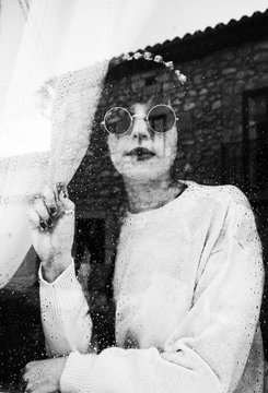 Retrato de una chica joven a través de un cristal de una ventana con gotas de agua  y aspecto triste 