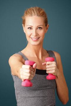 Fitness. Portrait of an attractive blond woman working out with dumbbell weights, toning her biceps while standing against isolated background. 