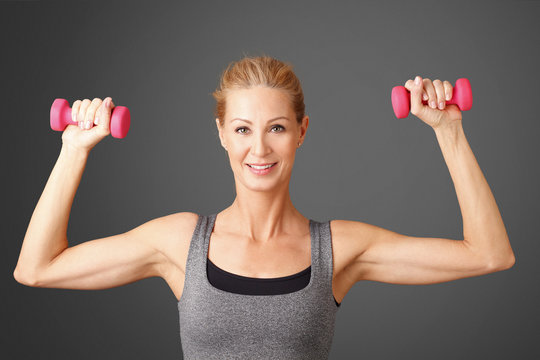 Fitness. Portrait of an attractive blond woman working out with dumbbell weights, toning her biceps while standing against isolated background. 