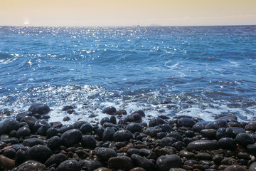 Obraz premium Black rock beach with blue sea at sunset on Santorini, Greek island.
