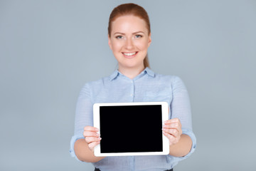 Your text is here. Beautiful young woman holding tablet and smiling while standing against grey background. Copy space 