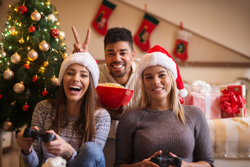 Beautiful young friends having fun, playing video games on Christmas.