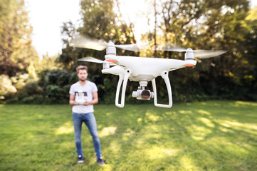 Young hipster man with flying drone. Sunny green nature.