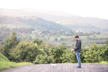 Young hipster man with flying drone. Sunny green nature.