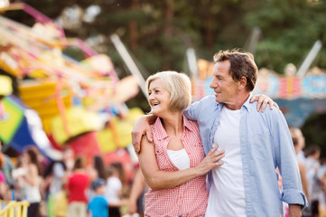 Senior couple at the fun fair, hugging. Sunny summer.
