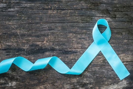 Light blue ribbon symbolic sign for prostate cancer awareness campaign and men's health in November on grunge old wood background: Shiny blue satin texture textile on dark wooden backdrop