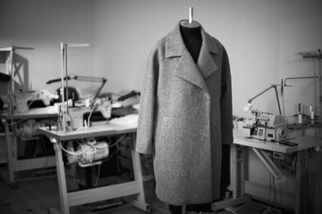 black and white photo with a coat on a mannequin in a sewing wor