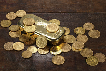 Goldbarren mit verschiedenen europäischen Goldmünzen aus dem 19./20. Jahrhundert auf rustikalem Holztisch