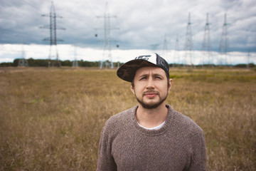 Courageous young man in cap on meadow, power pylons at background