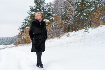 Fototapeta na wymiar The girl walks on a snow trail along the shore and woods