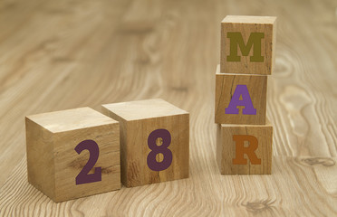 Cube shape calendar for March 28 on wooden surface.