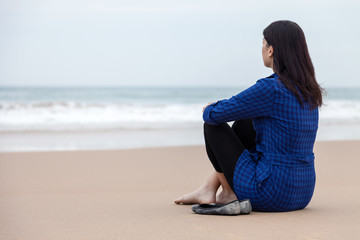 Lonely and depressed woman sitting on the sand of a deserted beach and watching the sea on an Autumn day.
