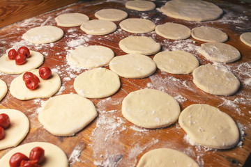 Preparing homemade ukrainian dumplings or varenyky, cutting the round pieces of dough with cherry