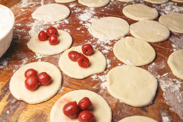 Preparing homemade ukrainian dumplings or varenyky, cutting the round pieces of dough with cherry