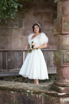 Bride poses with pink flowers under stone arch