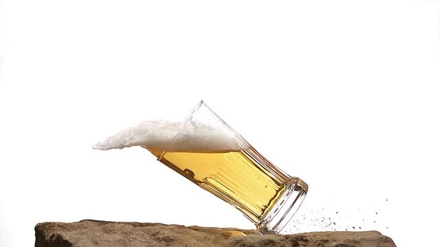 Glass of Beer falling and Splashing on Stone against White Background, Slow motion