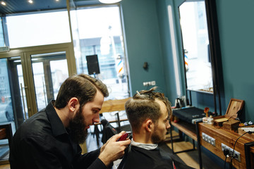 Male hairdresser cuts client electric clippers in the barbershop