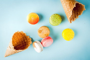 Multicolored macaroon cookies with ice cream cones on a blue background, top view, copy space
