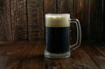 Dark beer mug with drops on wood background
