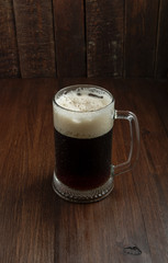 Dark beer mug with drops on wood background. Top view