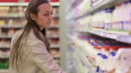 Young woman in a dairy section of supermarket choosing a bottle of milk.