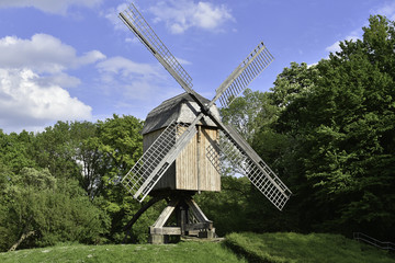 Obraz premium old wooden windmill on a background of trees and blue sky