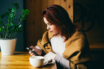 attractive young woman reading the news on the phone and drinking coffee