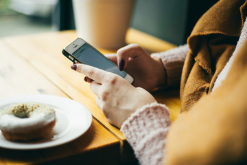 attractive young woman reading the news on the phone and eating a donut. hand closeup