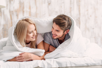 Joyful lovers relaxing under bedding quilt