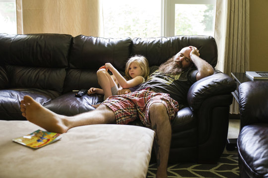 Girl looking away while sitting with father sleeping on sofa